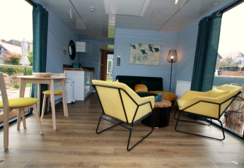 Moderne woonkamer op Houseboat Friedrich met gele stoelen, eettafel en grote ramen met uitzicht.
