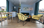 Moderne woonkamer op Houseboat Friedrich met gele stoelen, ronde tafel en grote ramen met zicht buiten.