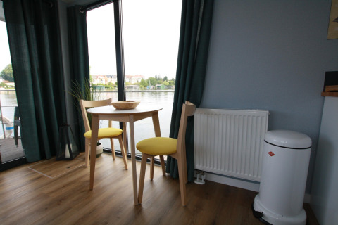 Lille spiseplads med to stole og bord på Houseboat Friedrich, udsigt over vandet gennem store vinduer.