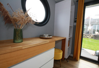 Interni moderni di Houseboat Friedrich con finestra tonda, scrivania in legno, sgabello giallo e vista giardino.