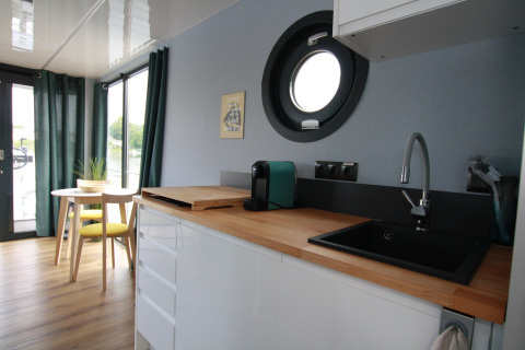 Cuisine moderne et coin repas sur Houseboat Friedrich avec hublot rond, plan de travail en bois et fenêtre.