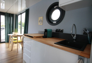 Cuisine moderne et coin repas sur Houseboat Friedrich avec hublot rond, plan de travail en bois et fenêtre.