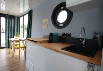 Cuisine moderne et coin repas sur Houseboat Friedrich avec hublot rond, plan de travail en bois et fenêtre.