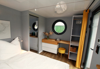 Gezellige slaapkamer op Houseboat Friedrich met rond raam, bureau, modern meubilair en warme tinten.