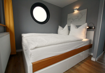 Modern slaapkamerinterieur op Houseboat Friedrich met rond raam, grijze muren en wit bed met houtaccent.