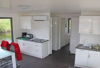 Interior de una casa flotante moderna con cocina blanca, mesa de comedor y vista al agua por grandes ventanas.