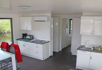Modern houseboat interior featuring a white kitchen, dining table and water view through large windows.