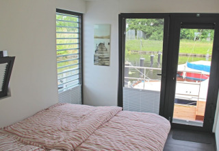 Camera da letto su una casa galleggiante con grandi finestre, vista sull'acqua e barche, letto a righe.
