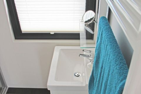 Cuarto de baño pequeño en una casa flotante, con lavabo blanco, toalla azul y ventana con persiana.