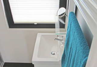 Bagno compatto su una casa galleggiante con lavabo bianco, asciugamano blu e finestra con persiana.