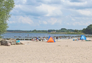 Strandscene med familier, små telte og udsigt over vandet fra Houseboat «Floating 44 Undine» i Tyskland.