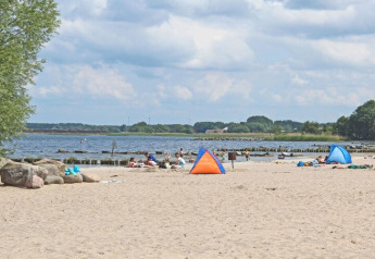 Zandstrand met gezinnen, kleine tentjes en zicht op het water vanaf Houseboat «Floating 44 Undine» in Duitsland.