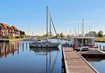Woonboot Floating 44 Undine voor vier personen aangemeerd aan een steiger in Duitsland op zonnige dag.