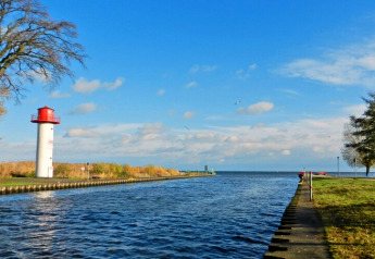 Zicht vanaf een woonboot op een waterweg met vuurtoren in Duitsland onder een heldere hemel.