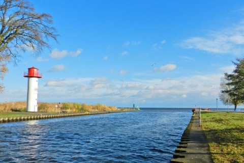 Vista da una casa galleggiante su un canale con faro in Germania sotto un cielo azzurro.