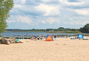 Strandansicht mit Menschen, kleinen Zelten und Meerblick unter teilweise bewölktem Himmel.