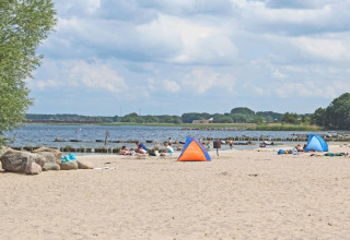 Beach scene with people, small tents, sandy shore, and a partly cloudy sky by the sea.