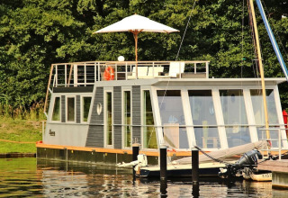 Modern houseboat with large windows and rooftop deck with parasol, docked at Houseboat Xenia in Germany.