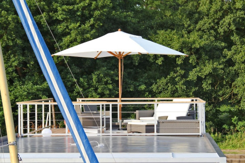 Rooftop terrace on houseboat 'Xenia' in Germany, featuring outdoor seating, umbrella, and trees backdrop.