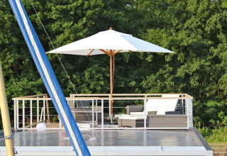 Rooftop terrace on houseboat 'Xenia' in Germany, featuring outdoor seating, umbrella, and trees backdrop.