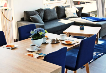 Helles, modernes Esszimmer auf Hausboot Xenia in Deutschland mit blauen Stühlen und grauem Sofa.
