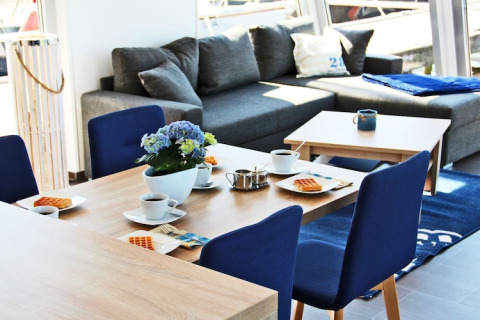 Bright, modern dining area on Houseboat Xenia in Germany with blue chairs, grey sofa, and breakfast setup.