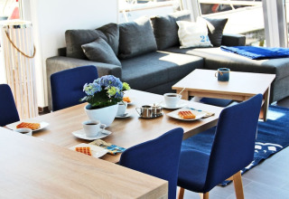 Bright, modern dining area on Houseboat Xenia in Germany with blue chairs, grey sofa, and breakfast setup.