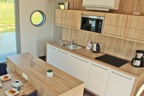 Modern kitchen area on houseboat Xenia in Germany featuring wooden finish, appliances, and a porthole window.