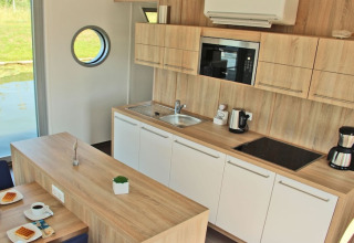 Modern kitchen area on houseboat Xenia in Germany featuring wooden finish, appliances, and a porthole window.