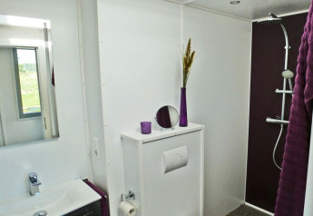 Moderne badkamer op woonboot Xenia in Duitsland met paarse accenten, douche en witte muren.