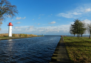 View from houseboat 'Xenia' in Germany with lighthouse, canal, trees and a bright blue sky.