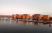 Photo de péniches modernes amarrées dans une marina paisible, leurs reflets sur l’eau au coucher du soleil.