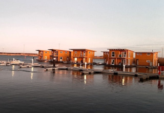 Foto van moderne woonboten aangemeerd in een rustige haven, met hun reflectie zichtbaar in het water.