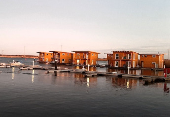 Immagine di moderne case galleggianti ormeggiate in un porto turistico tranquillo, illuminate dal tramonto.
