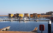 Photo of modern houseboats docked at a marina, with wooden piers and calm water on a clear day.