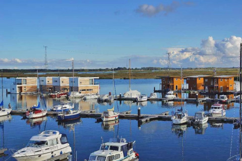 Woonboten en plezierboten in een kalme haven met een uitgestrekt landschap en blauwe hemel op de achtergrond.