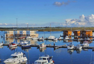 Woonboten en plezierboten in een kalme haven met een uitgestrekt landschap en blauwe hemel op de achtergrond.