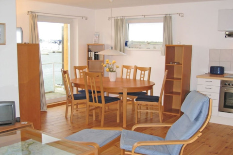Interior de casa flotante con mesa de comedor, seis sillas, grandes ventanas y vistas panorámicas al agua.
