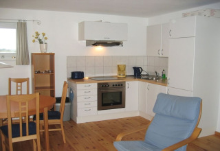 Woonkeuken op een woonboot met houten meubels, witte kasten, eettafel en comfortabele fauteuil.