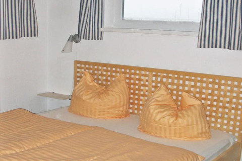 Et soveværelse på en husbåd med orange sengetøj, stribede gardiner og tremmegavl ved vinduet.
