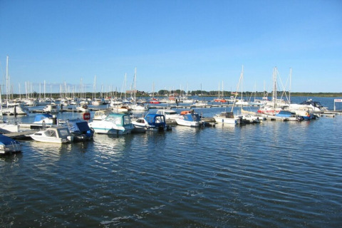 Boten en woonboten liggen in een haven op een zonnige dag met blauwe lucht en rustig water.