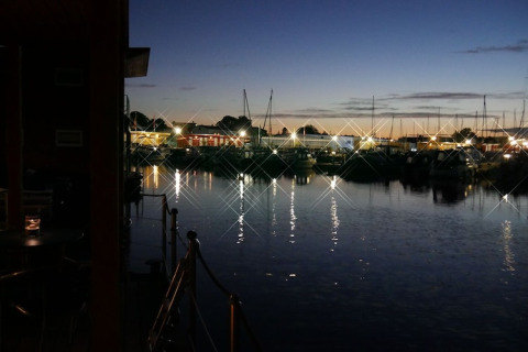 Avondfoto vanaf een woonboot met uitzicht op de jachthaven, verlicht door weerkaatsende lichten.