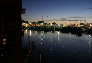 Avondfoto vanaf een woonboot met uitzicht op de jachthaven, verlicht door weerkaatsende lichten.