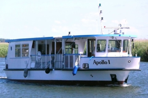 Een witte woonboot met de naam Apollo I vaart op een rivier, omringd door groene natuur en blauwe lucht.