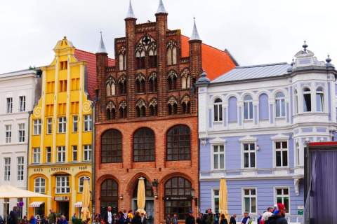Coloridos edificios históricos y cafés con gente paseando y sentada en una animada plaza urbana.
