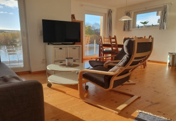 Living room on a houseboat featuring an armchair, sofa, TV, and dining area with scenic waterfront views.