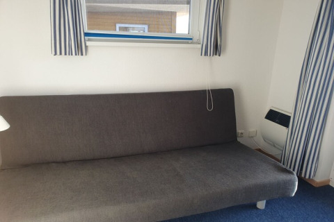 Gray sofa bed under a window with blue and white striped curtains, on a houseboat with blue carpet flooring.