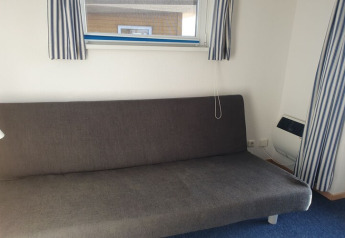 Gray sofa bed under a window with blue and white striped curtains, on a houseboat with blue carpet flooring.