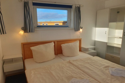 Bedroom on a houseboat with a double bed, white furniture, striped curtains, and a bright window view.