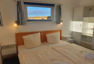 Schlafzimmer mit Doppelbett, weißen Möbeln und Fensterblick, aufgenommen auf einem modernen Hausboot.
